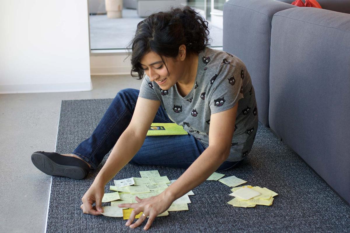 Aminder Dhaliwal candidly sitting on a sofa and arranging various drawn post-its notes.