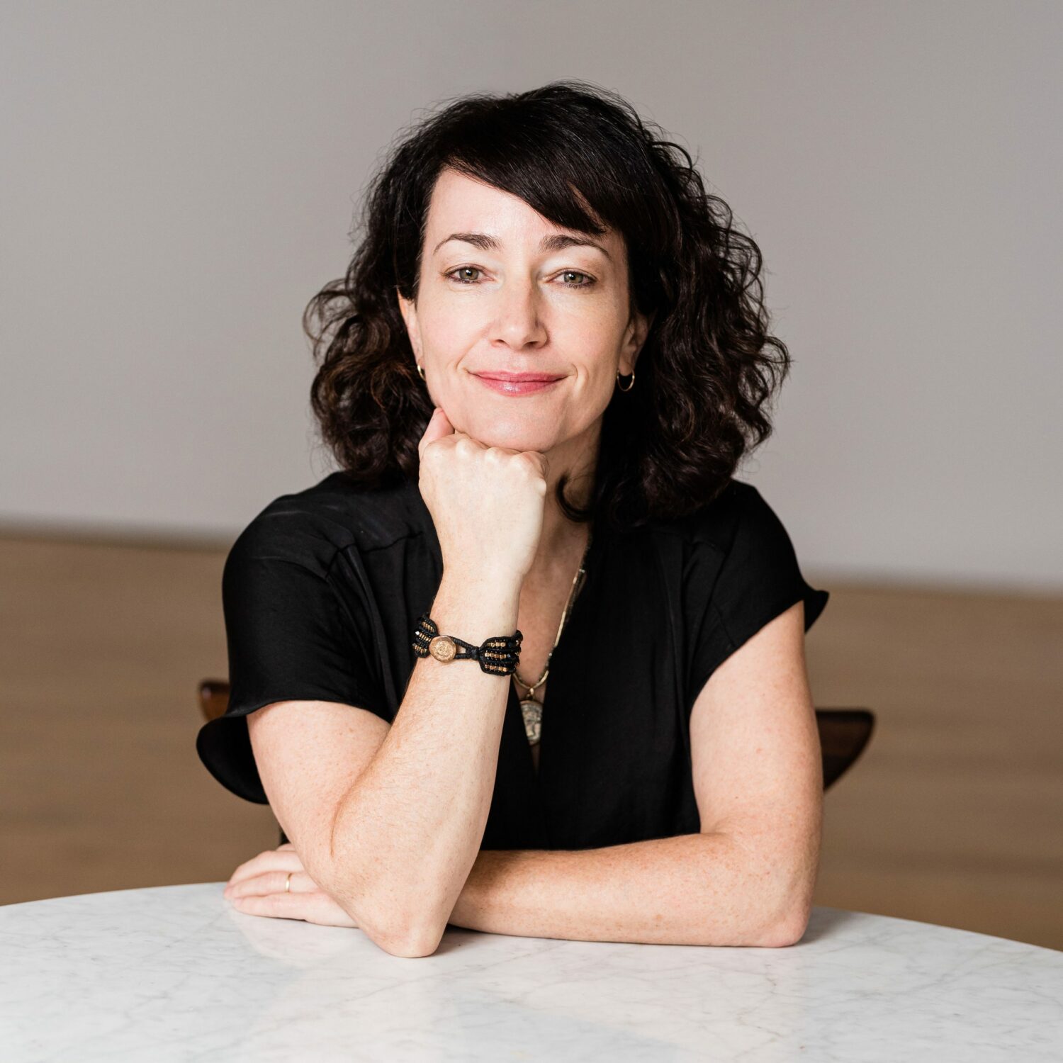 Author photo of Leslie Hurtig sitting behind a desk, with one arm up supporting her chin.