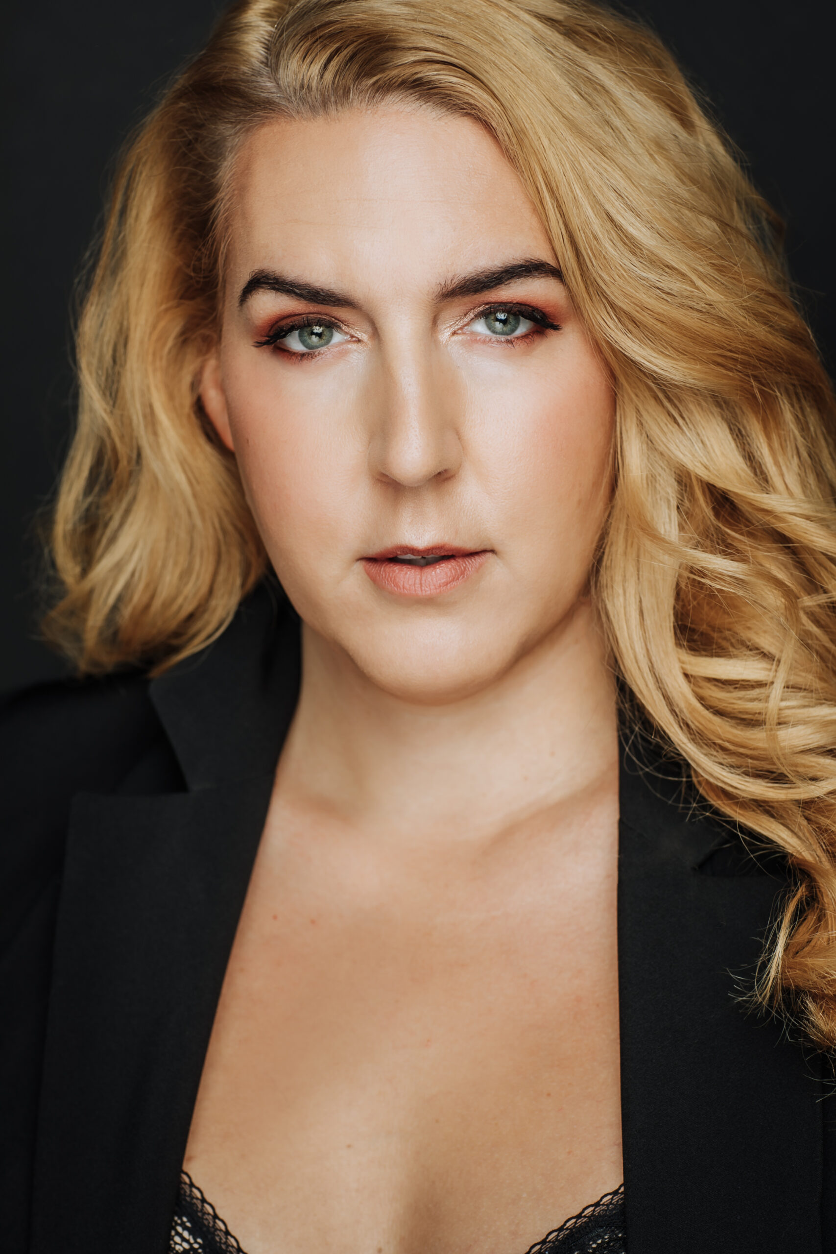 A headshot of Luna Ferguson. They have shoulder length blonde hair and are wearing a black blazer.