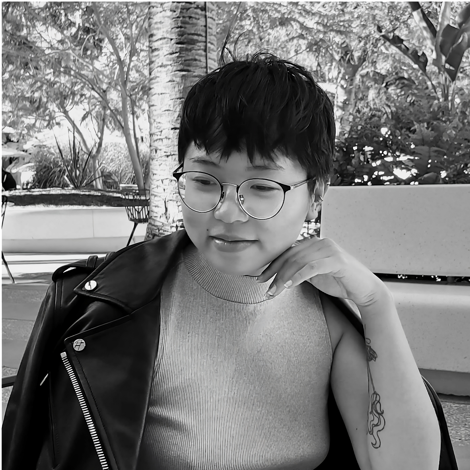2-1 A black and white photo of K. Quyen Pham. She has short black hair and glasses, and poses with her left hand to her chin and a black jacket around her shoulders.