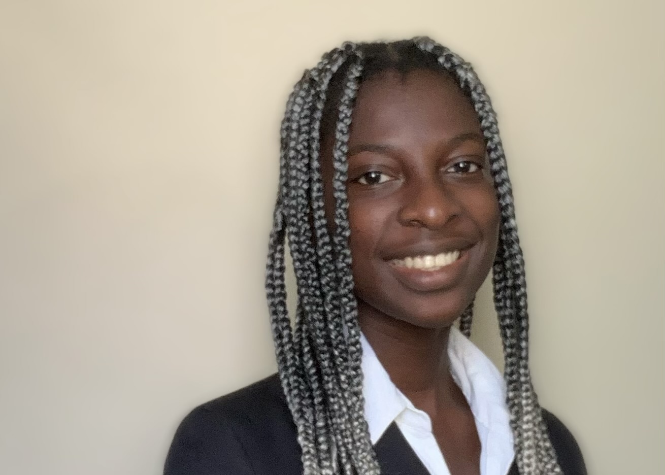 IMG_6518 A young Black woman with blond box braids, a white blouse, and a black blazer smiles at the camera.