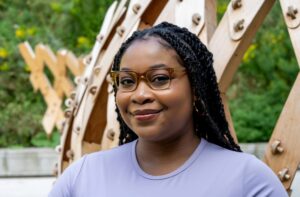 A photo of Terese Mason Pierre from the shoulders up. She is a Black woman with her hair in braids wearing caramel-coloured glasses and a lavender-coloured shirt.